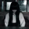 薄暗い室内で俯く長い黒髪の女性の不気味な表情