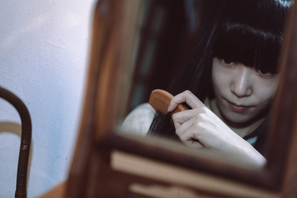 薄暗い鏡の前で櫛を通す前髪パッツンの女性