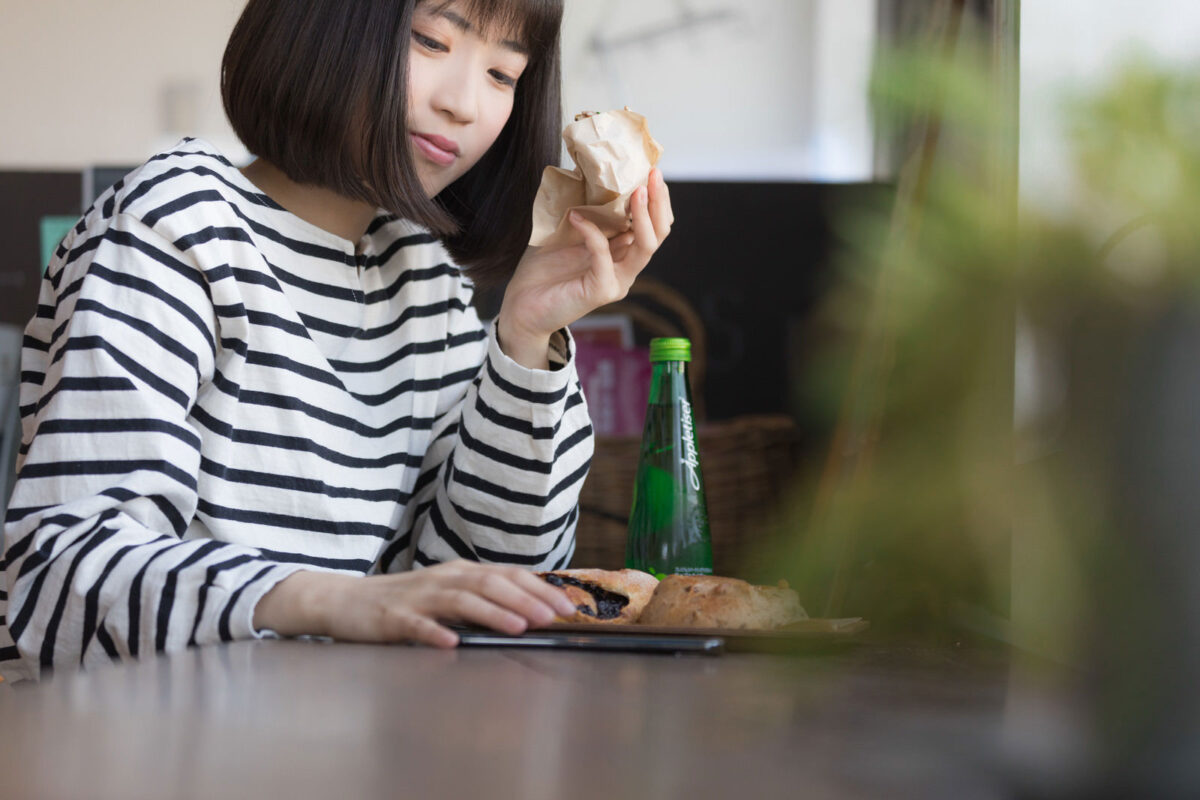 フードコートでパンを食べながらスマホを見る女性