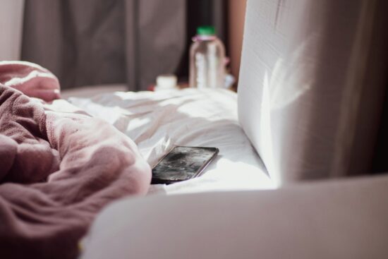 朝の光が差すベッドの上、ピンクの毛布のそばに置かれたスマホ